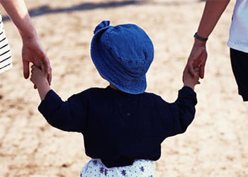 Small girl with a blue hat holding the hands of both of her parents, symbolizing child custody and divorce.