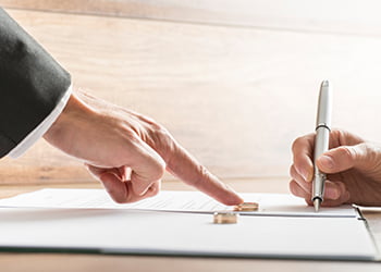 Man pointing at his gold wedding ring as individual writes documents in relation to divorce and child custody.